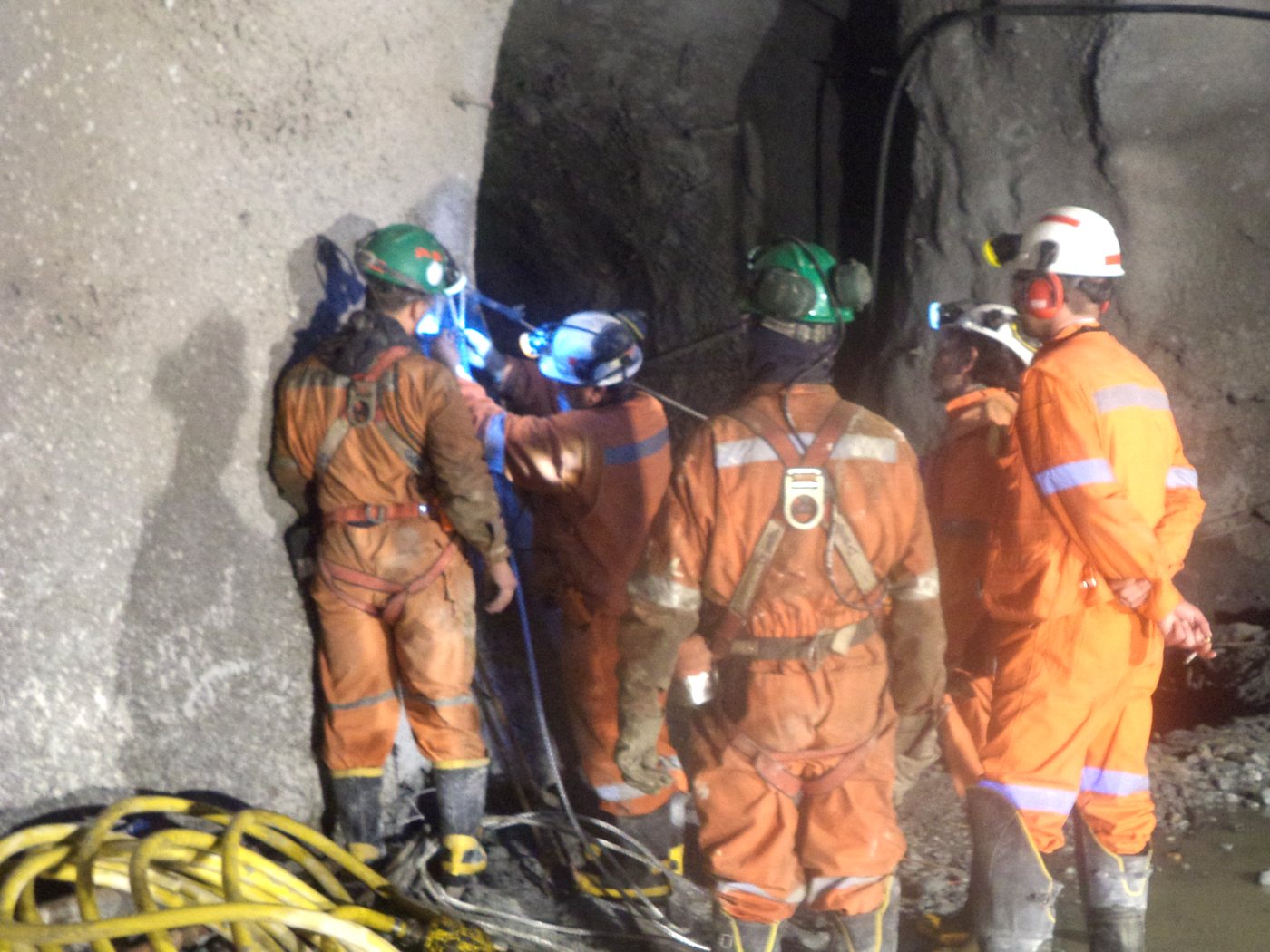 Mineros chilenos con equipo de protección personal completo —overol con cintas reflectantes, casco, protección auditiva y arnés— ejecutando trabajos en faena